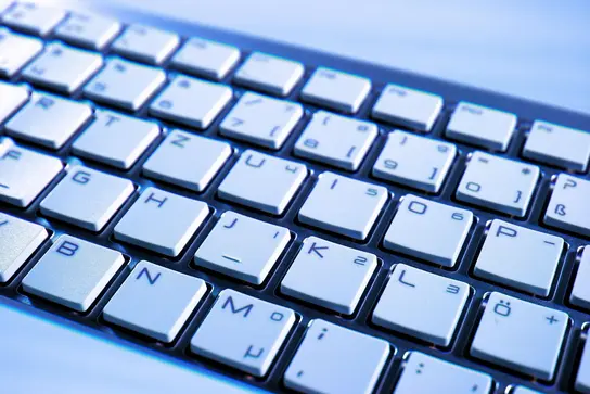 Close-up of a modern computer keyboard, featuring silver keys with black letters and symbols. The image highlights the arrangement of the keys, suitable for typing, reflecting a sleek and functional design often used in technology and computing environments.