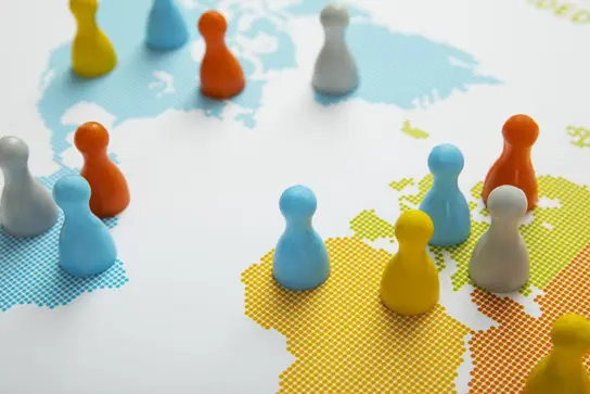 A colorful arrangement of game pieces in various shapes is placed on a map, highlighting different regions. The pieces are in blue, yellow, orange, and white, symbolizing players or regions on the map's dotted design.