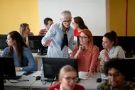 Professorin erklärt Studentinnen etwas an einem Bildschirm.