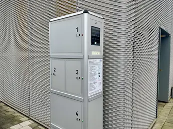 A metal charging cabinet for e-bikes is mounted on the exterior wall of a metal building.