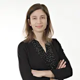 A woman with medium-length brown hair stands confidently with her arms crossed. She is wearing a black shirt with a polka dot pattern and is facing the camera, conveying a professional demeanor against a light background.
