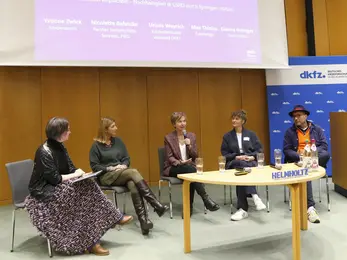 Four panelists and a moderator sit on stage, engaging in a discussion.