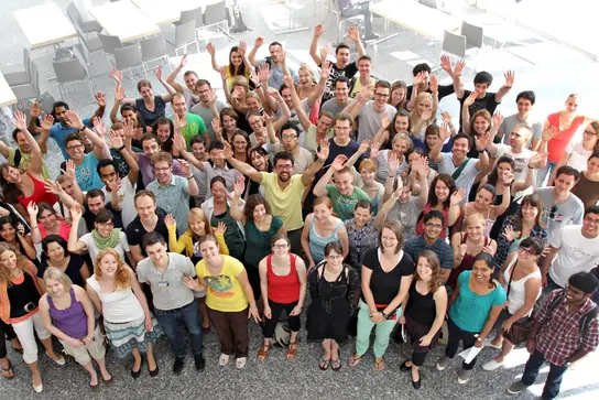 A group of PhD students waving at the camera and smiling.