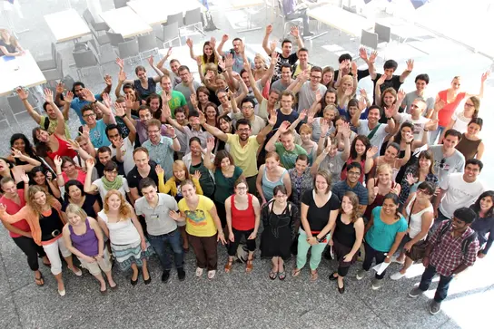 A group of PhD students waving at the camera and smiling.