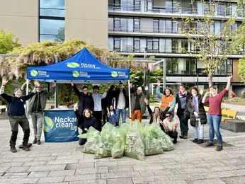 A group stands in front of a tent with bags of collected trash, raising their hands in celebration.