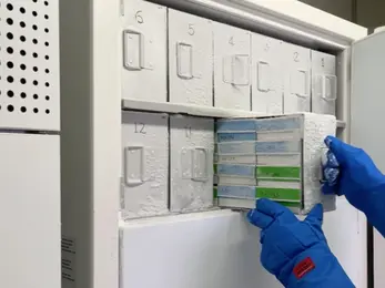 A lab member wearing blue cold-resistant gloves pulls metal racks from an ULT freezer, showcasing the well-organized storage space.