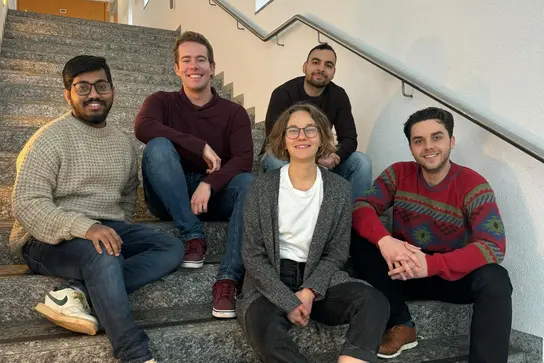 Five members of the 2025 PhD Council are seated on a staircase.