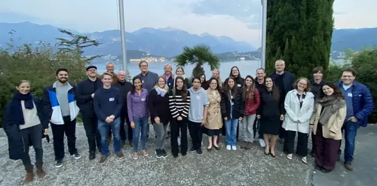 A group of 26 people are standing in front of Lake Como.