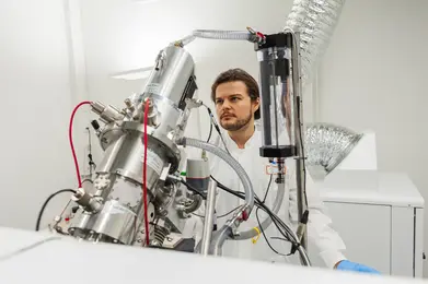 A scientist in a white lab coat stands at an advanced scientific instrument in a laboratory. The device is complex, featuring metallic components and various tubes. The scientist appears focused and engaged with the equipment, which is part of ongoing research in the field of immunology and single-cell biology.