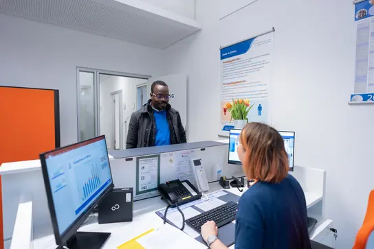 A woman sits at a reception desk while a man enters.