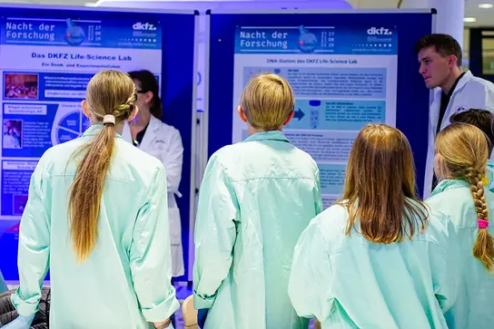 Jugendliche stehen vor einer Wand mit zwei Plakaten mit naturwissenschaftlichem Inhalt.