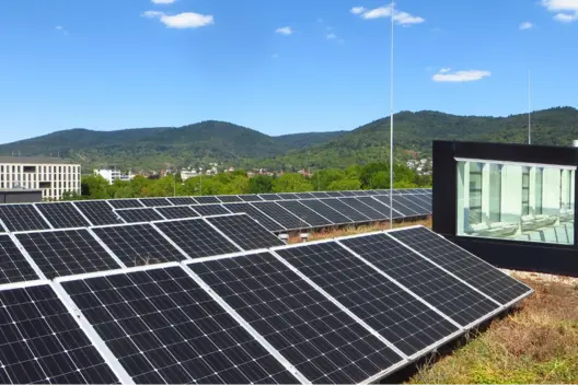 Solarmodule auf dem Dach eines modernen Gebäudes an einem sonnigen Tag, mit bewaldeten Hügeln im Hintergrund