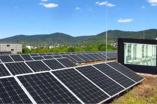 Solarmodule auf dem Dach eines modernen Gebäudes an einem sonnigen Tag, mit bewaldeten Hügeln im Hintergrund